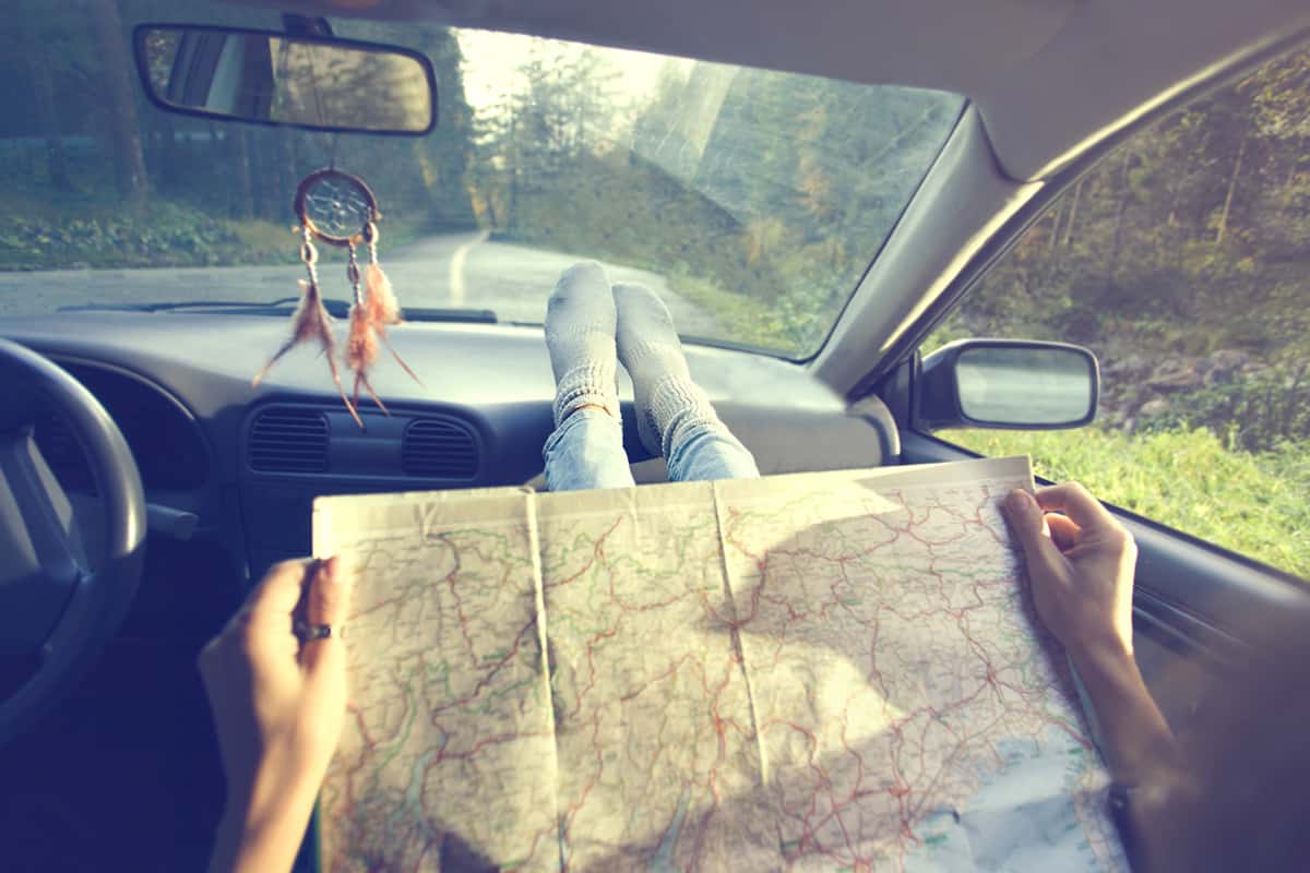 En person sitter i bilen med fötterna på instrumentpanelen och läser en gammal karta