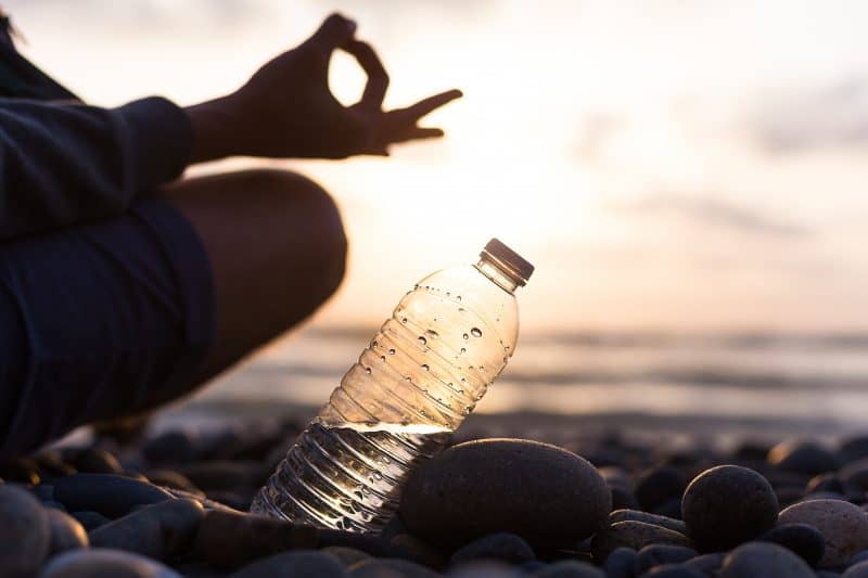 Plastic bottle of water near man, boy doing yoga on the beach at sunset , sunrise time. Yoga finger pose