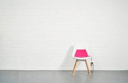 The heated pad Heather in the color pink on a white chair with a white brick background.