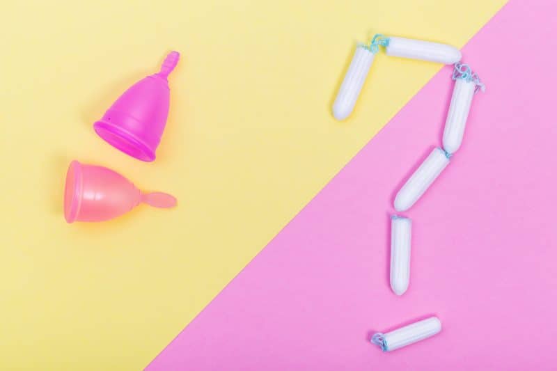 Pink menstrual cup and tampons on color paper background, female intimate hygiene period products, top view